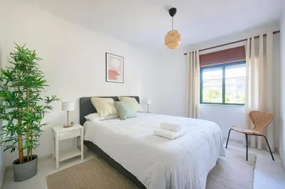 a white bedroom with a large bed and a plant at 2 Bedroom by Quarteira Beach in Quarteira
