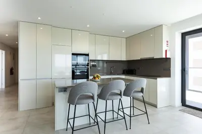 a kitchen with white cabinets and bar stools at Terracos de Quarteira II Pearl by Real Properties in Quarteira