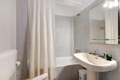 a white bathroom with a sink and a shower curtain at Beachfront Apartment T2 in Quarteira
