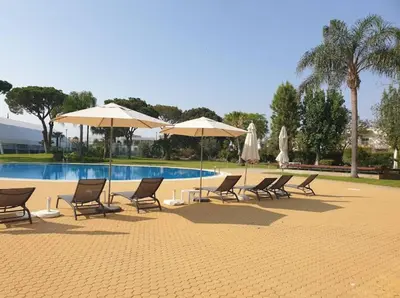 a group of chairs and umbrellas next to a pool at Modern apartment in Al-sakia Village in Quarteira