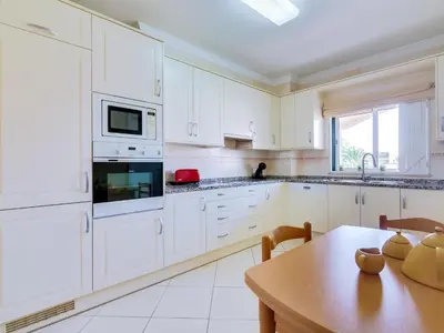 a kitchen with white cabinets and a wooden table at 1 bdr apartment with pool next to Laguna Golf Course in Vilamoura