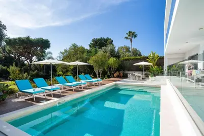 a swimming pool with blue chairs and umbrellas at Deluxe Ancao in Almancil