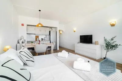 a bedroom with a white bed and a kitchen at Alamos - Dream Lodging in Albufeira
