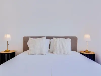 a white bed with white pillows and two lamps at T2 Moderno e Renovado a 500m da praia de Quarteira in Quarteira