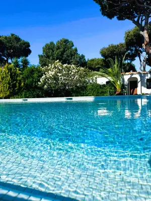 a blue swimming pool with trees in the background at Solar dos Pinheiros T3 in Vilamoura