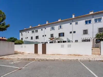 a white building with a fence and a parking lot at Duplex T2 com terraço e BBQ em Vilamoura in Quarteira