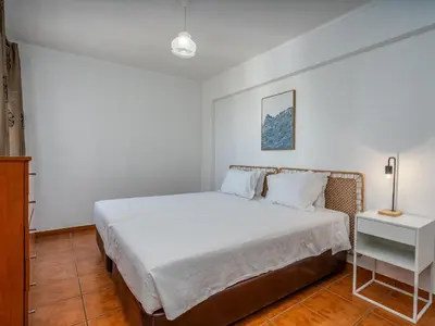 a white bedroom with a bed and a night stand at T1 com Varanda e vista mar a 200m da Praia in Quarteira