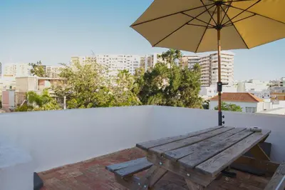 a wooden picnic table with an umbrella on a roof at Guest House Mercado in Faro