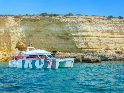 a boat in the water next to a cliff at Ocean Breeze Rooms, Albufeira in Albufeira