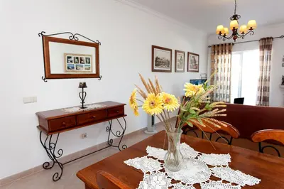 a living room with a vase of flowers on a table at Os Apartamentos A Ramos na Praia da Galé Estão inserido em Condomínio com PISCINA, Fica apenas a 350 Metros da Praia da Galé - Apartamentos com Ar Condicionado tanto nos Quartos como na Sala, Smart TV com Prime Vídeo e Cozinha Completa in Albufeira