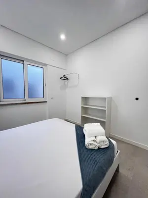 a white bedroom with a bed and two windows at Cantinho da Paz in Faro
