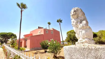 a statue in front of a red building with palm trees at Vila Paraiso da Maria 5 quartos duas salas, jardim, piscina, varanda com churrasqueira e WIFI in Olhos de Água