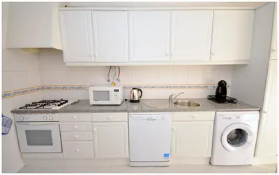 a kitchen with white cabinets and a washer and dryer at Apartamentos Capitolina in Quarteira