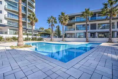 a swimming pool in front of a building with palm trees at Cavalo Preto Beach Resort Apt & Wi-Fi Nr Beach in Quarteira