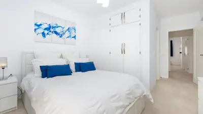 a white bedroom with a large white bed with blue pillows at Lounge Garden Apartment in Vilamoura