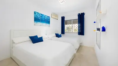 two beds in a white room with blue curtains at Lounge Garden Apartment in Vilamoura