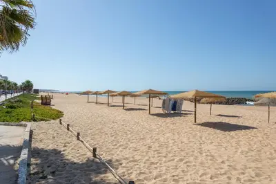 a row of umbrellas on a beach with the ocean at AL - Apartamentos Vista Mar in Quarteira