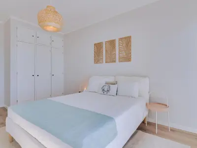 a white bedroom with a large bed and a table at Apartamento Vida Pura com 2 quartos e vista mar in Quarteira