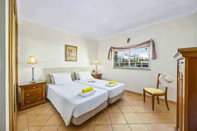 a bedroom with two beds and a window and a chair at Villa Anthony by Villa Plus in Terras Novas