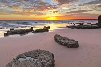 a sunset on a beach with rocks in the sand at Condo-Pool walk to the Beach by Algarve Dream Holidays in Albufeira