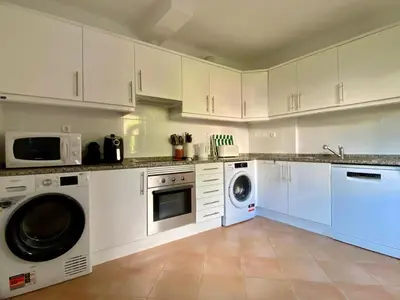 a kitchen with white cabinets and a washer and dryer at Casa Manacá Vilamoura in Quarteira