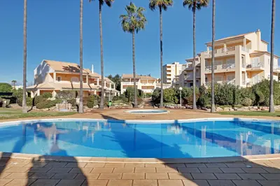 a swimming pool in front of a building with palm trees at Las Palmeiras Vilamoura in Quarteira