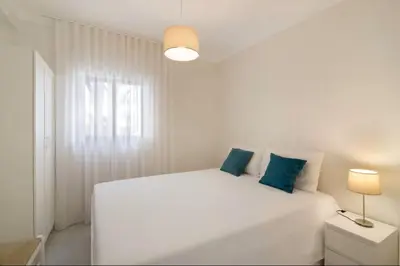 a white bedroom with a large white bed with blue pillows at Apartment Jardins da Falesia in Roja- Pé