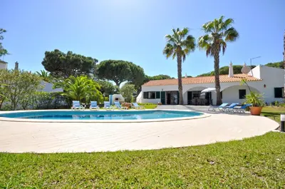 a swimming pool in front of a house with palm trees at Casa da Palmeira in Quarteira