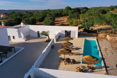 an outdoor patio with chairs and umbrellas and a pool at Uma Casa Rural in Santa Bárbara de Nexe