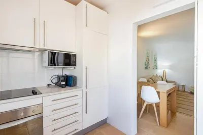 a kitchen with white cabinets and a table with a chair at Salgados Retreat -Steps from the Beach at Homesbyfc in Guia