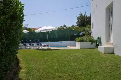 a yard with chairs and an umbrella next to a pool at Villa Jose in Olhos de Água