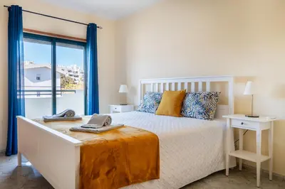 a bedroom with a white bed with blue curtains at Apartamento Norte by Férias com Sol in Quarteira