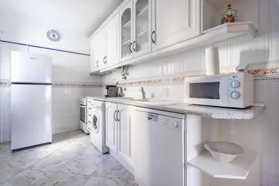 a white kitchen with a sink and a microwave at Apartamento Norte by Férias com Sol in Quarteira