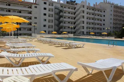 a row of white chairs and umbrellas next to a pool at Cheerfulway Minichoro Apartamentos in Albufeira