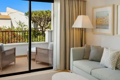a bedroom with a bed and chairs and a balcony at Pine Cliffs Ocean Suites, a Luxury Collection Resort & Spa, Algarve in Albufeira