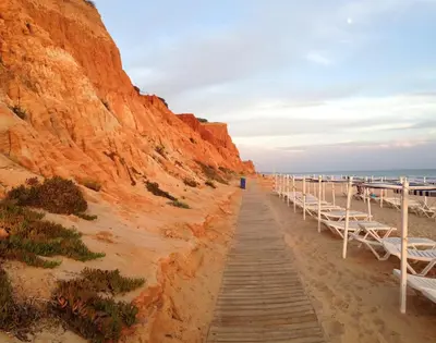 a wooden boardwalk on the beach next to a cliff at Albufeira Falesia Beach Apartment in Albufeira