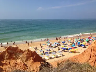 a group of people on a beach with umbrellas and the ocean at Albufeira Falesia Beach Apartment in Albufeira