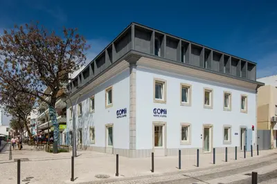 a white building with a black roof on a street at Hostel Conii & Suites Algarve in Quarteira