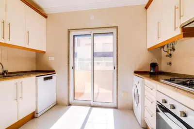 a kitchen with white cabinets and a sliding glass door at AL- Apartamentos Novos Vista Mar in Quarteira