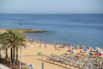 a crowd of people on a beach with umbrellas at AL- Apartamentos Novos Vista Mar in Quarteira