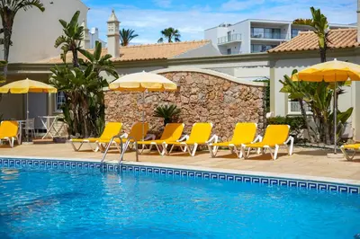 a pool with chairs and umbrellas next to a building at Vila do Castelo in Albufeira
