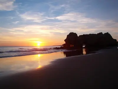 a sunset on a beach with rocks and the ocean at Vila Branca in Mosqueira