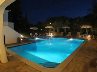 a swimming pool with chairs and an umbrella at night at Casa Camelia in Vilamoura