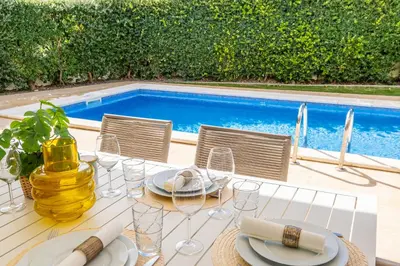a table with plates and glasses next to a pool at Villas Novochoro - Large Garden- Heatable Pool by DreamvillasAlbufeira in Albufeira