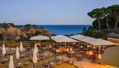 a restaurant with white umbrellas and chairs and the ocean at 3HB Falésia Garden in Albufeira