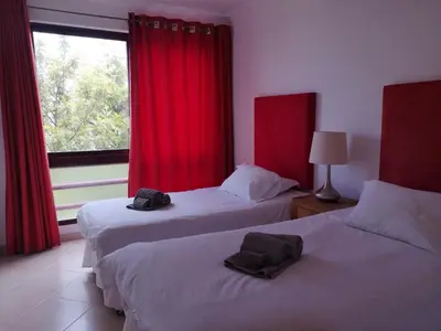 two beds in a room with red curtains and a window at Mare Viva Beach Apartment in Quarteira