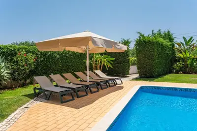 a group of chairs and an umbrella next to a swimming pool at Fonte Santa Villa in Quarteira