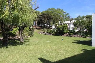 a yard with green grass and trees and a house at By the Beach in Almancil