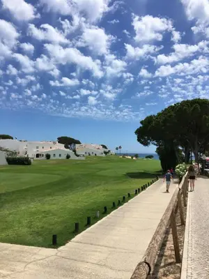 two people walking down a sidewalk next to a green field at Vale Do Lobo 935 in Loulé