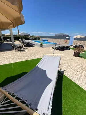 a hammock on a beach with a surfboard and an umbrella at Sunfield Guest House - Only Adults in Albufeira